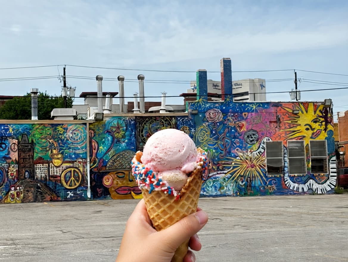Someone holding an ice cream cone in front of the murals in Deep Ellum