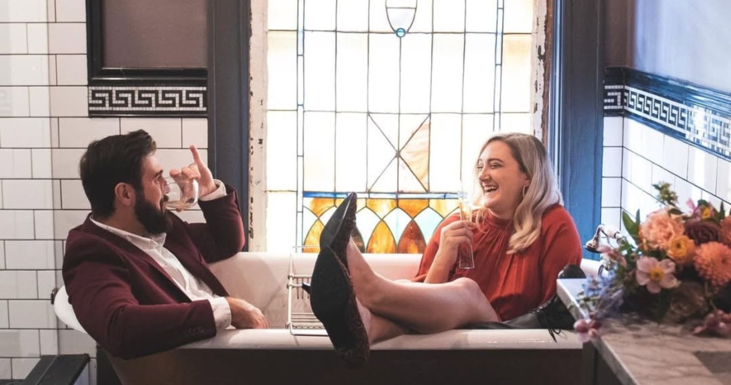 A couple sipping cocktails in the clawfoot tub at our Dallas bed and breakfast during a romantic weekend getaway